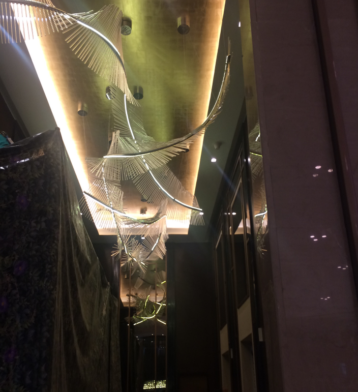 A luxurious ceiling installation with golden lighting and intricate abstract metal designs, creating an artistic and elegant ambiance.