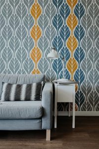 Stylish living room with a bold patterned wallpaper featuring blue, gray, and mustard yellow leaf motifs, paired with a modern gray sofa and a white side table.