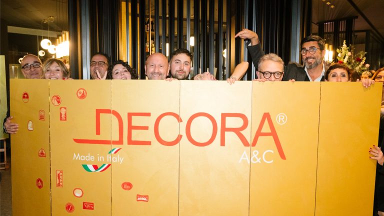 Group photo of smiling people holding a large "Decora" banner, with a "Made in Italy" logo.