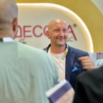 Smiling man in a blue blazer engaging in conversation at a Decora exhibition booth.