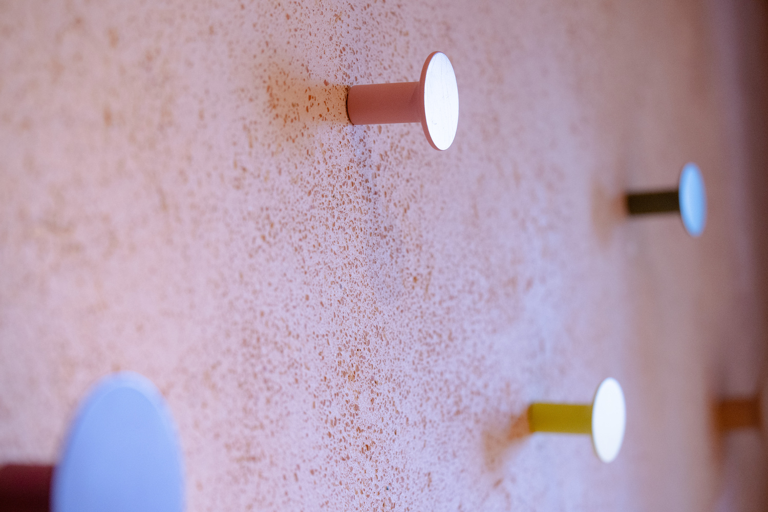 Modern wall hooks against a textured backdrop with a minimalistic design, featuring Cocciopesto-inspired colors from Decora A&C.