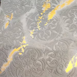 Close-up of a decorative cement stencil with ornate floral and geometric patterns, accented by gold streaks on a textured gray surface.