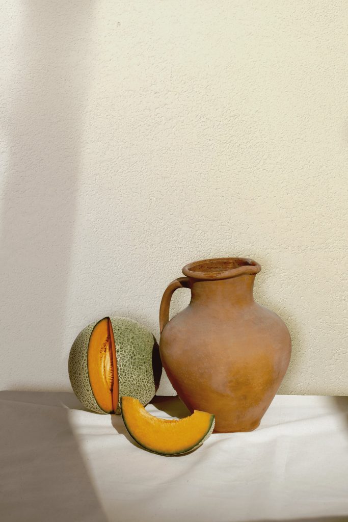 Clay jug with melon slices on a textured wall background showcasing lime-based paint.