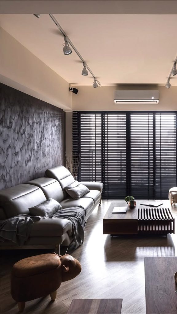 ERA by Decora’s modern minimalist living room featuring a gray leather sofa, textured accent wall, wood finishes, and natural light.
