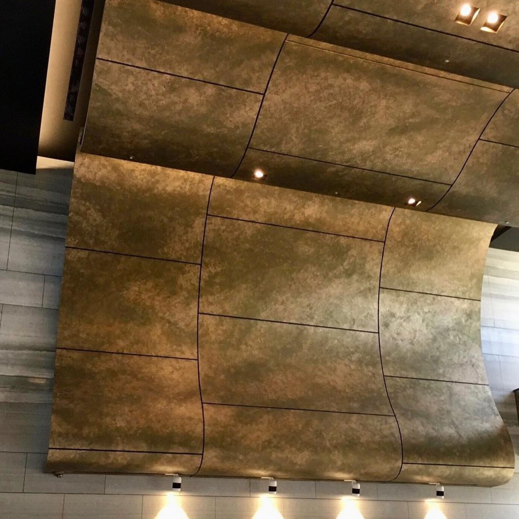 A curved luxury interior wall finished with a 3D sandy textured metallic paint in warm gold tones, illuminated by downlights.
