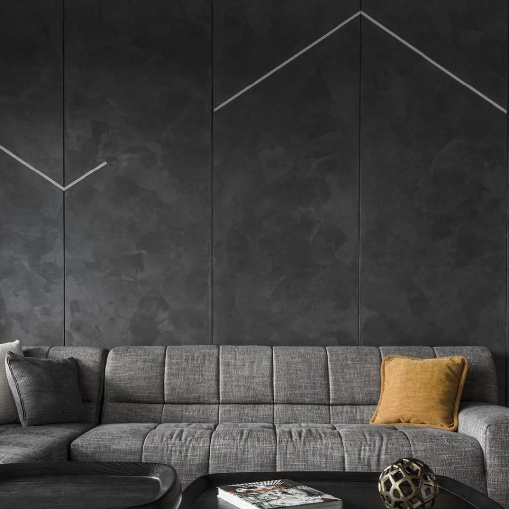 Contemporary living room with textured black Infinity metallic wall finish, featuring a soft shimmer and velvety metallic coating behind a minimalist gray sofa.