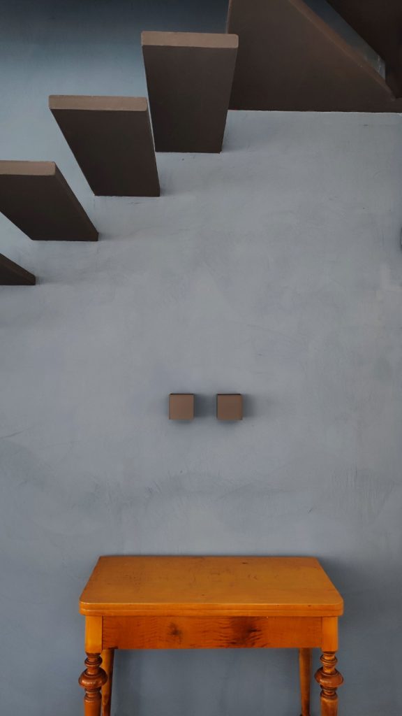 Modern floating staircase above a vintage wooden table against a smooth blue plaster wall.