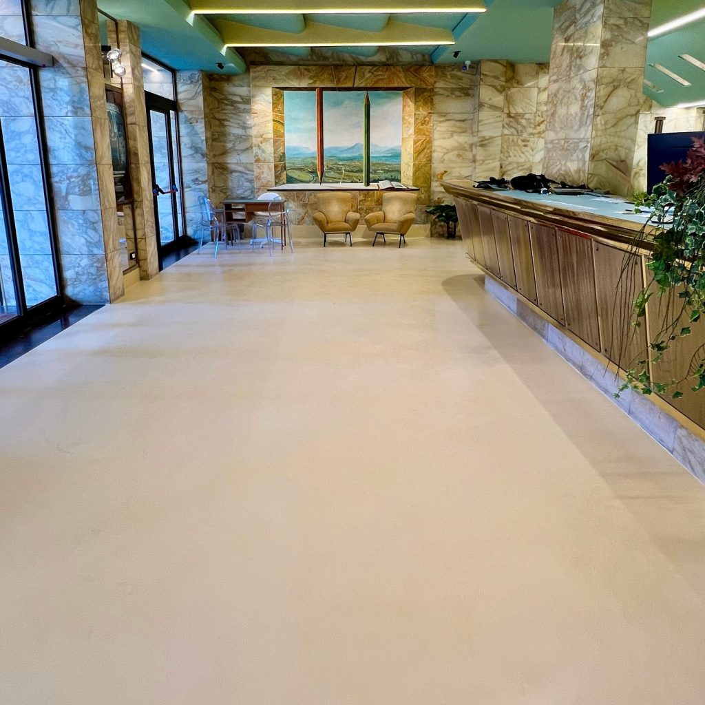 Seamless microcement floor by Decora at Cinema Fiamma reception with marble finishes and mural artwork
