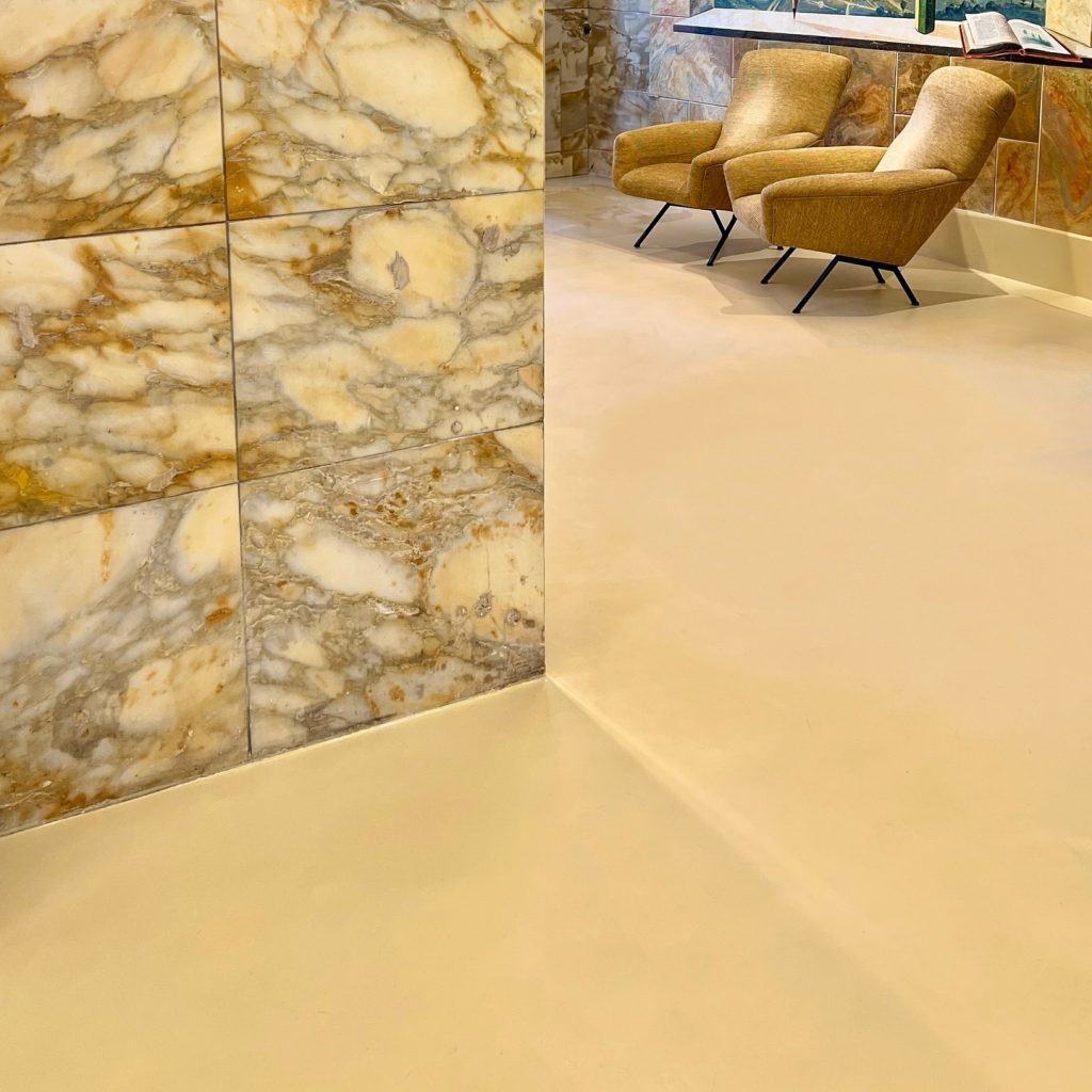 Seamless microcement floor by Decora with golden marble wall in a luxury interior