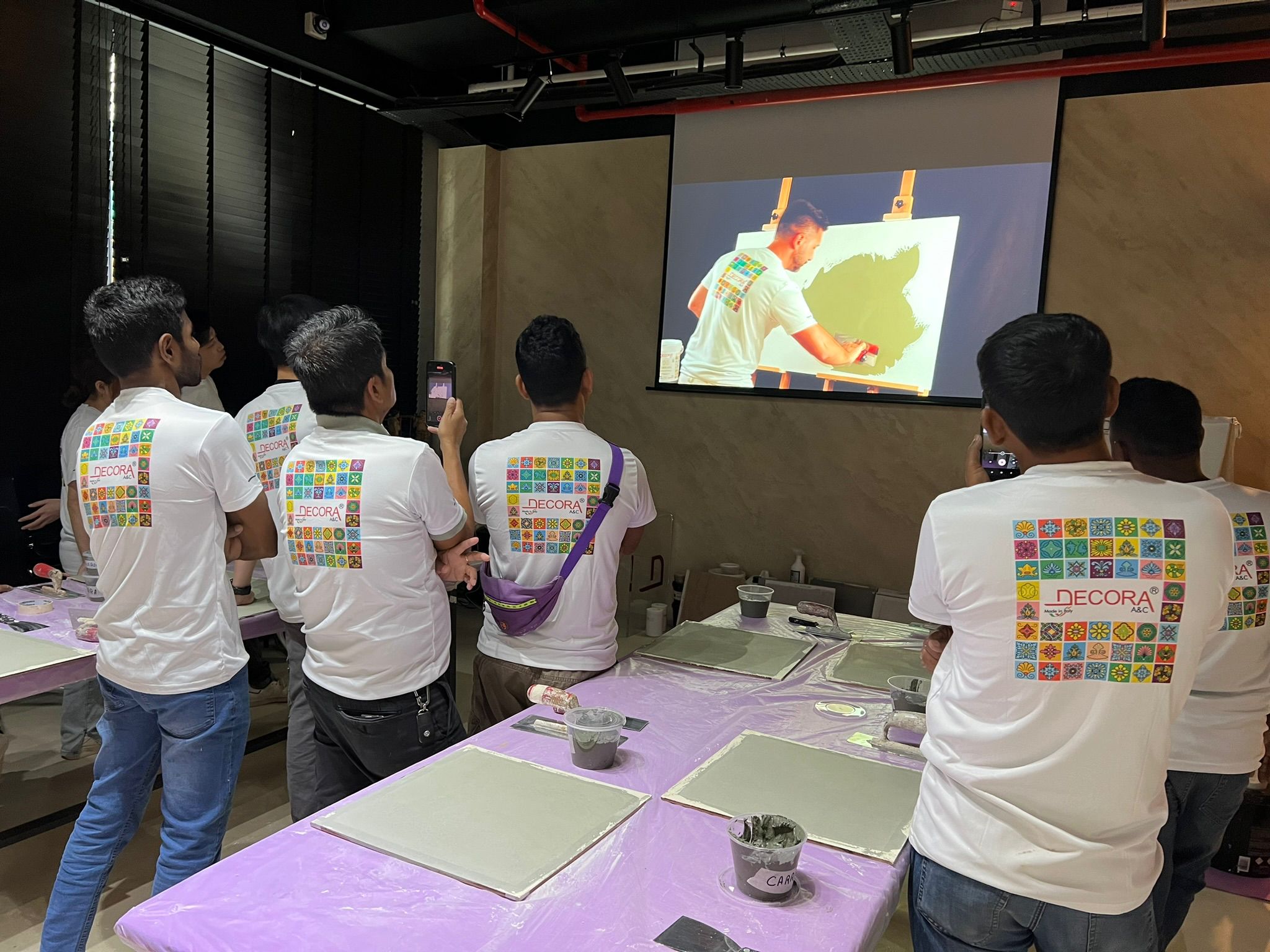 Happy participants at Decora Academy watch a demo on textured wall finishes, preparing to apply their own samples.
