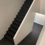 Minimalist staircase with black microcement steps and white side walls.