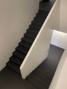 Minimalist staircase with black microcement steps and white side walls.