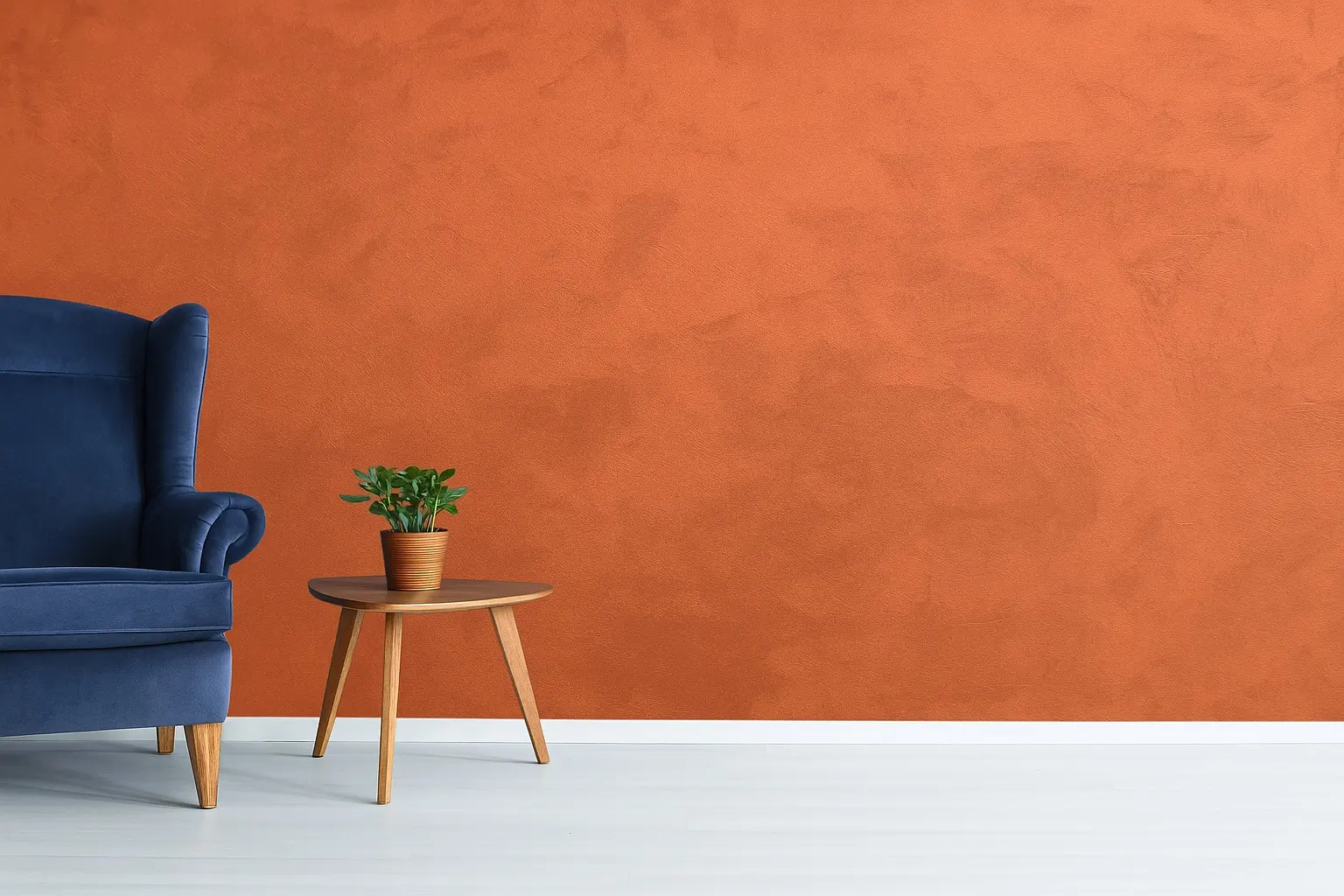 Terracotta feature wall with velvety decorative paint from the INFINITY collection by Decora A&C, paired with a blue velvet armchair and wooden side table