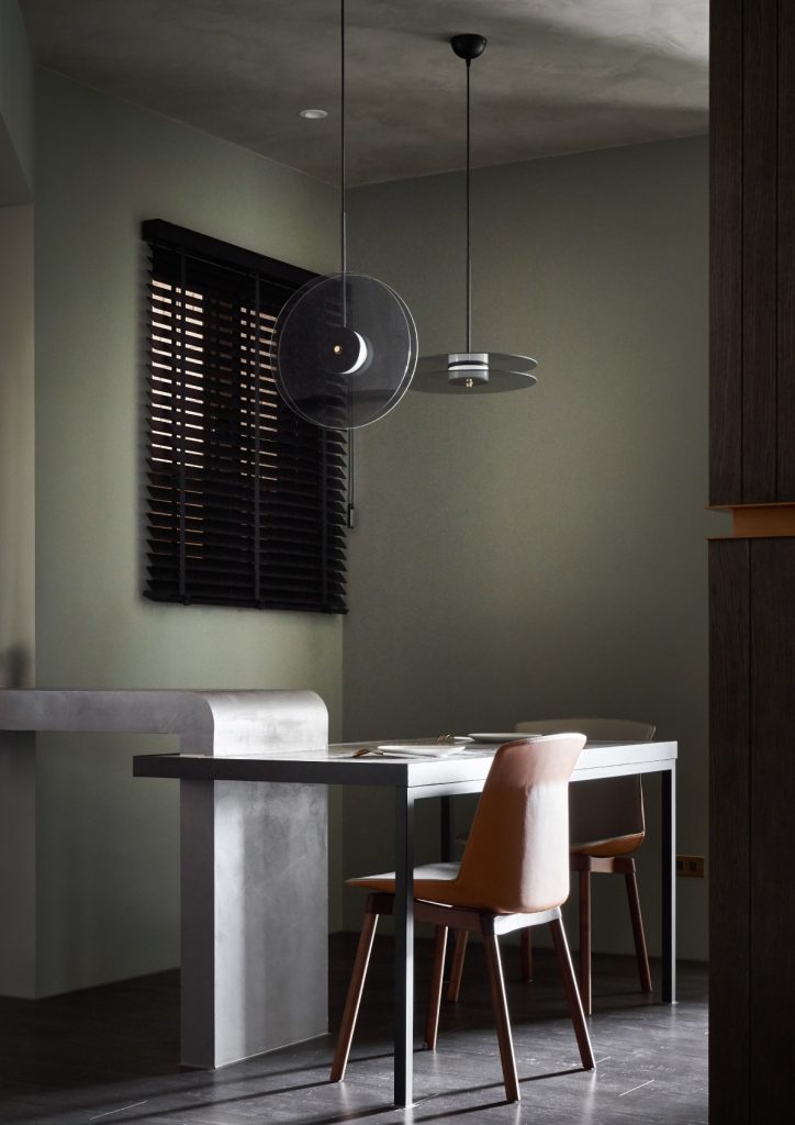 Modern dining space with a muted green lime-washed wall and industrial-style furnishings.